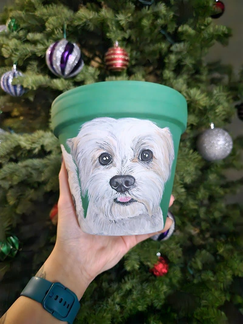 Hand-painted white terrier on a green clay pot in front of a Christmas tree