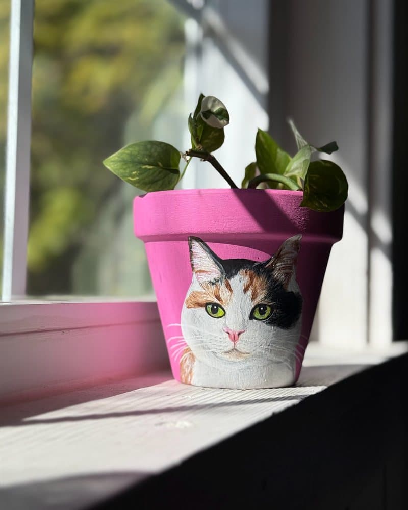 Hand-painted calico cat on a pink clay pot on a sunny windowsill