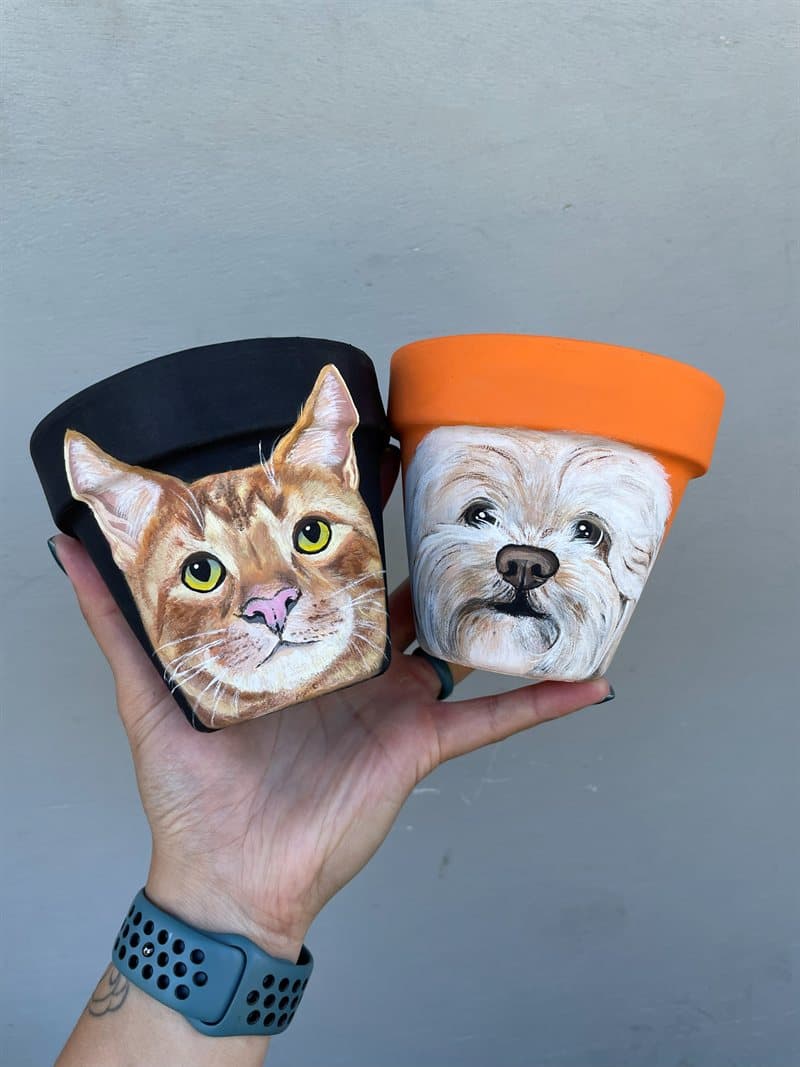 Two hand-painted pots — an orange tabby cat on black and a white dog on terracotta orange