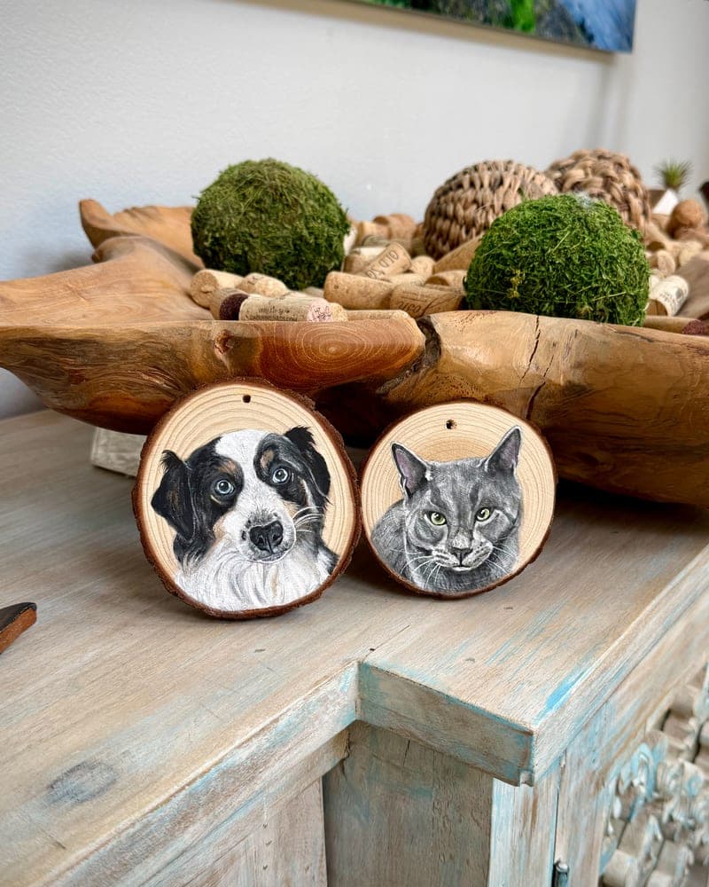 Two hand-painted wood round ornaments side by side — a black-and-white collie and a grey cat — on a weathered blue-washed sideboard