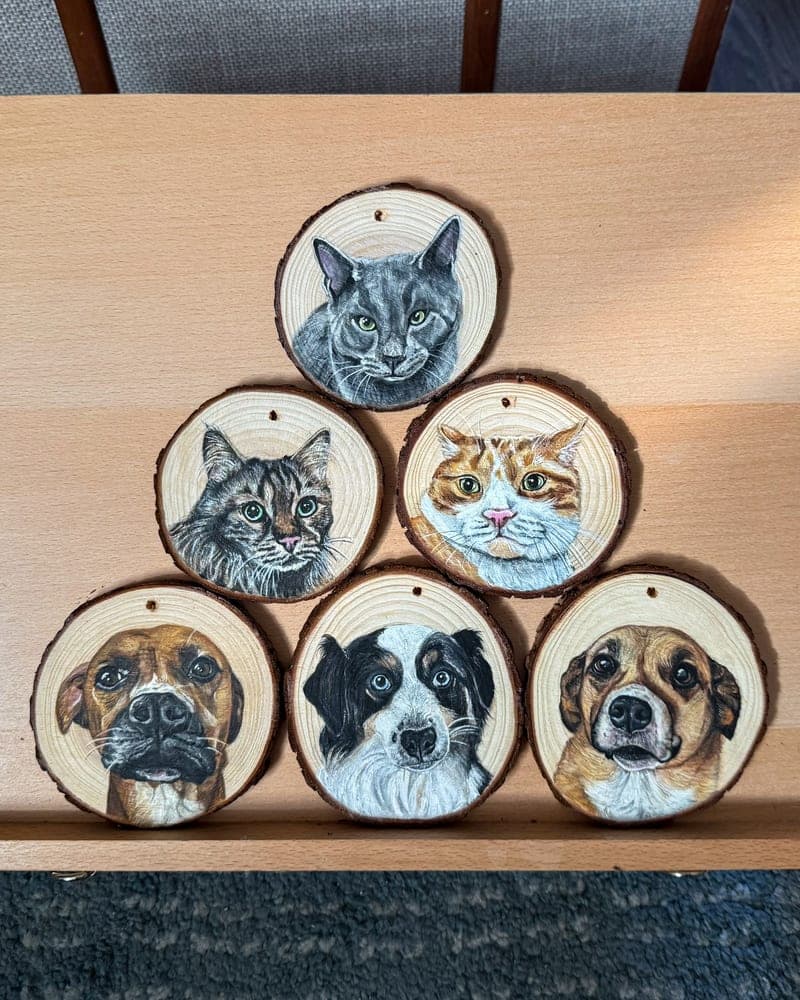 Six hand-painted wood round ornaments arranged in a pyramid — a grey cat, a brown tabby, an orange-and-white cat, a boxer, a black-and-white collie, and a tan dog