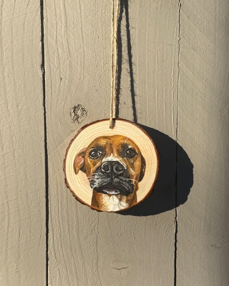 Hand-painted boxer on a wood round ornament, hanging by twine on a sunlit wooden fence