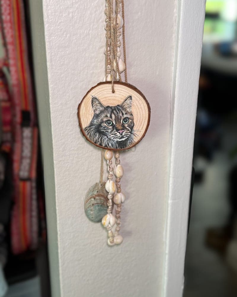 Hand-painted tabby cat on a wood round ornament, hanging on a white doorframe with a shell-and-bead strand