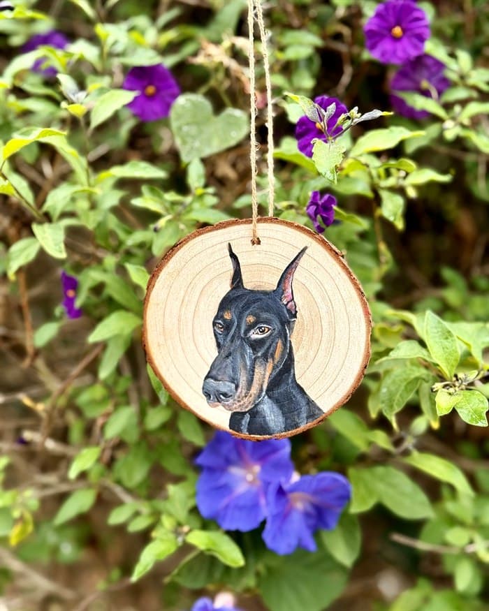 Example wood round — a Doberman painted on a slice of wood, hanging among flowers