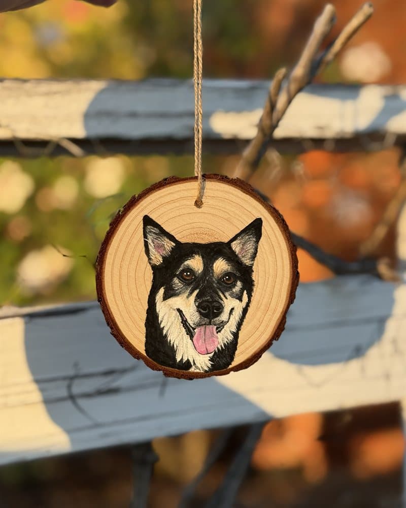 Hand-painted black-and-tan dog on a wood round ornament against a fence