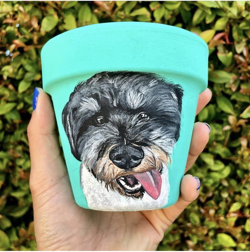 Hand-painted black schnauzer on a teal clay pot among greenery